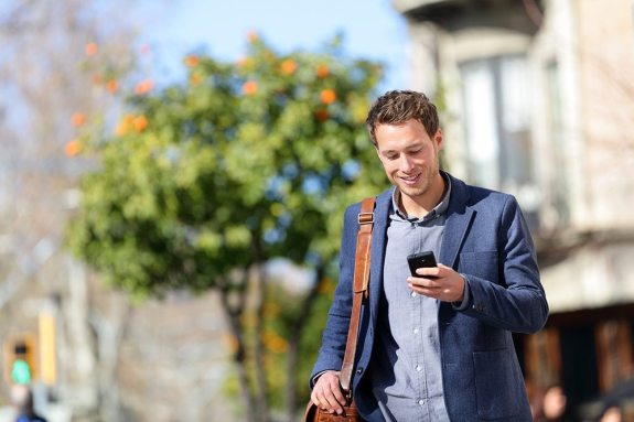 Young urban professional man using smart phone. Businessman holding mobile smartphone using app texting sms message wearing jacket on Passeig de Gracia, Barcelona, Catalonia, Spain.